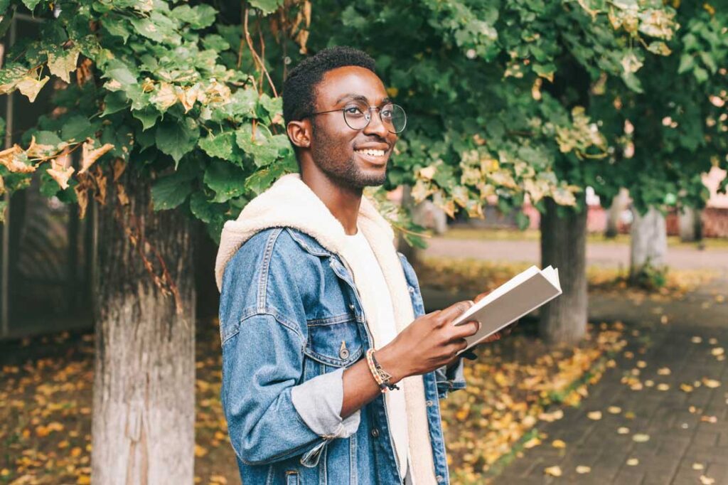 happy millennial man reading book outside