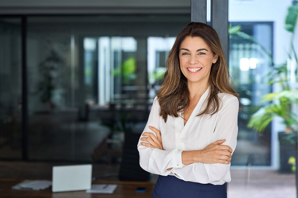 Confident business woman smiling standing in office arms crossed looking at camera