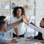 Happy manager high-fiving employees in office meeting