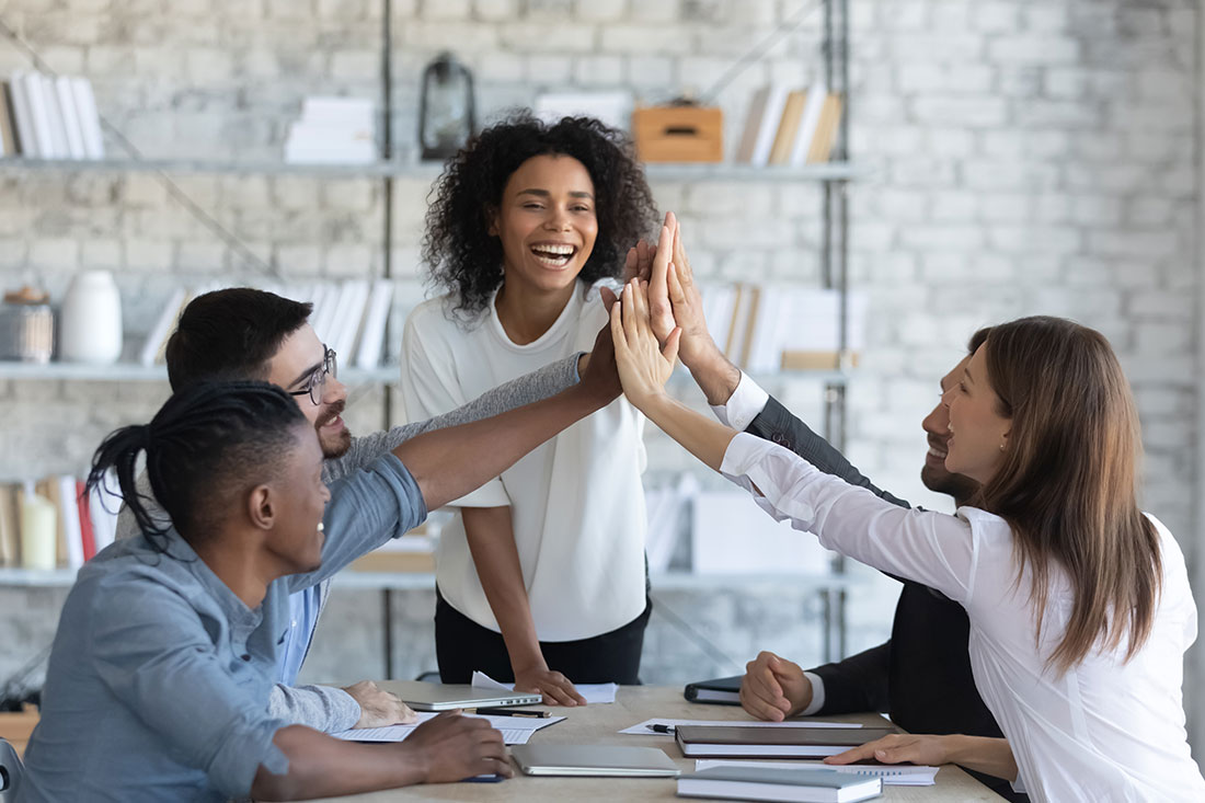 Happy manager high-fiving employees in office meeting