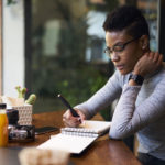 woman writing goals in journal at a cafe