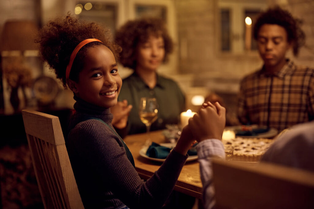 Young smiling girl at Thanksgiving dinner holding hands and giving thanks because this family is teaching kids gratitude