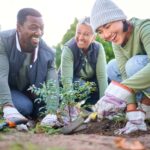 Three people smiling while gardening showing the benefits of volunteering