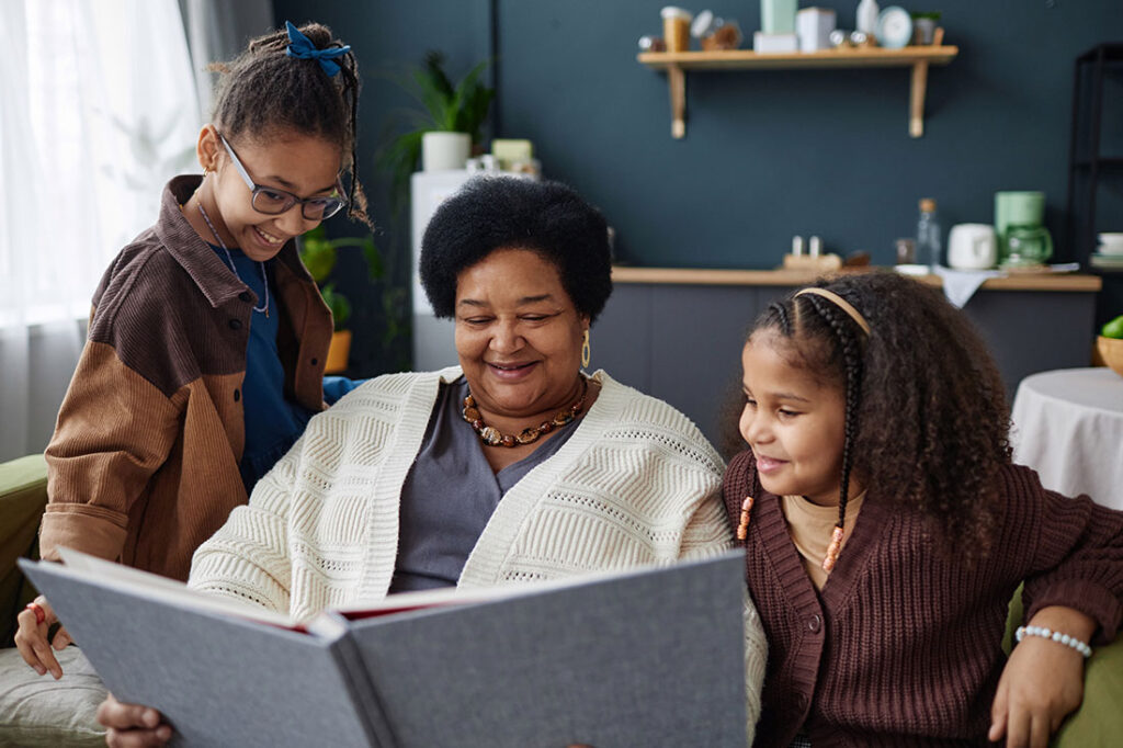 Smiling African American woman with two children looking at family photo album together at home