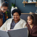 Smiling African American woman with two children looking at family photo album together at home