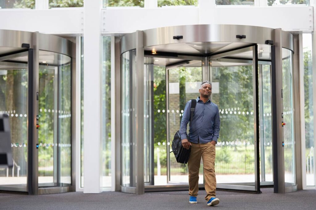 middle aged man walks through revolving doors to return to office, which could impact DEI efforts