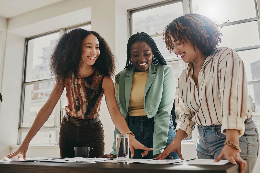 three women standing at a work table and smiling, a picture of workplace happiness