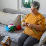 woman crocheting on a couch while watching a tutorial on her laptop