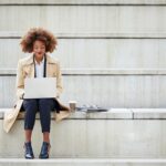 employee sitting on concrete steps working on her laptop