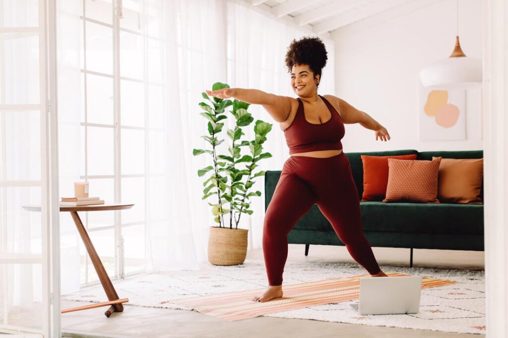 happy woman does yoga pose in her living room as part of a corporate wellness program