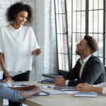 A young Black woman leading a team of 3 other employees at work while smiling to demonstrate her leadership soft skills