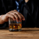 Close up photograph of a man in a suit with his hand over a glass of whiskey to symbolize quitting drinking