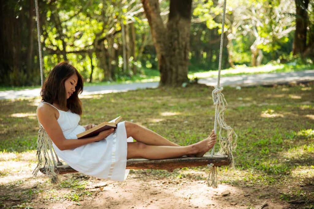 a young women lying on a bench in a park reading emotional intelligence books