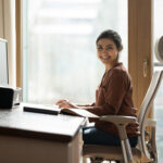 An Indian woman smiling and working at her ergonomic home office