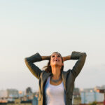 A business woman on a rooftop with the city in the background embracing failure and looking up towards the sky