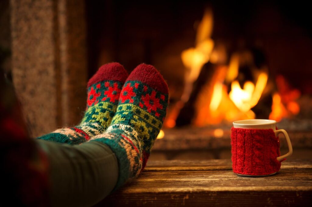 Two cozy feet in holidays socks in front of a fire to demonstrate what is hygge Christmas