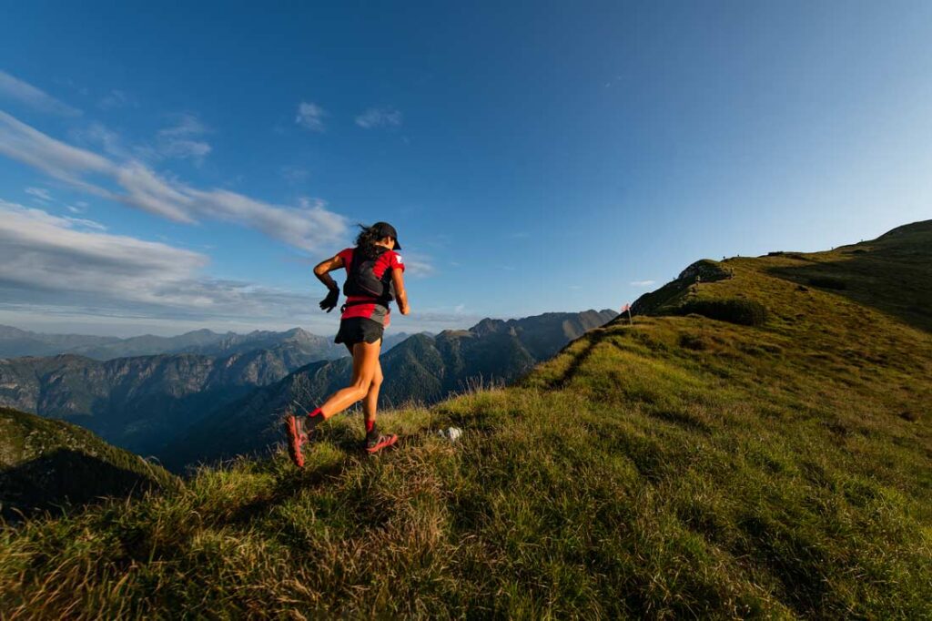 Woman trail running with beautiful mountain landscape in the background showing what ultra athletes can teach us about grit and perseverance