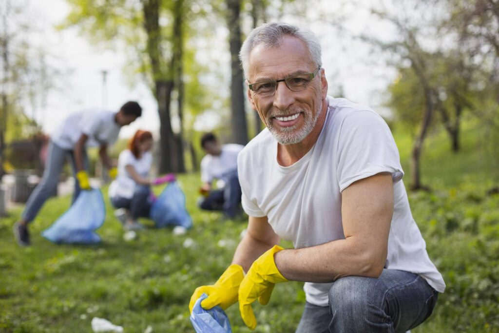 Senior man smiling picking up trash because he knows why volunteering is so important