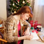 woman sitting at desk writing christmas cards and wondering how to politely stop sending christmas cards