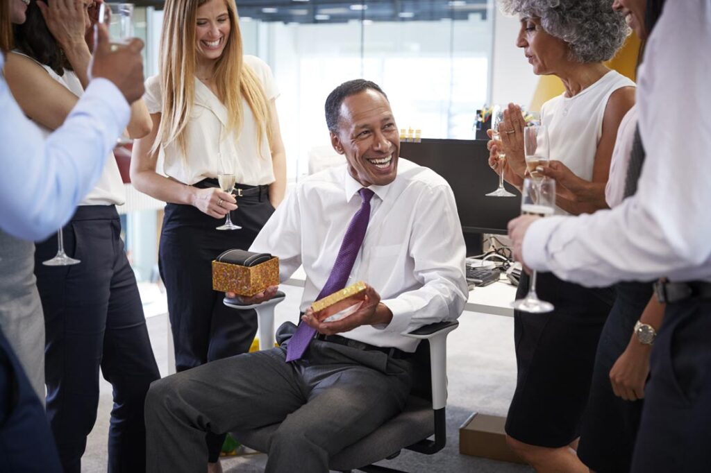 A man receiving a small gift from his coworkers and smiling because they chose the best gifts for coworkers