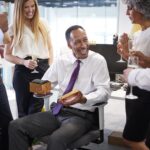 A man receiving a small gift from his coworkers and smiling because they chose the best gifts for coworkers