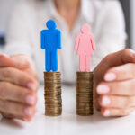 figurines of a man and a woman on top of a stack of pennies to represent the gender pay gap