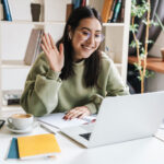 Young remote worker smiling and waving in a video call while she is building relationships with coworkers virtually