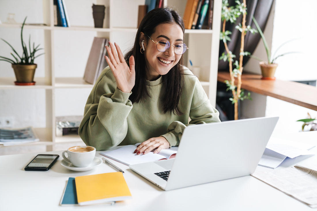 Young remote worker smiling and waving in a video call while she is building relationships with coworkers virtually