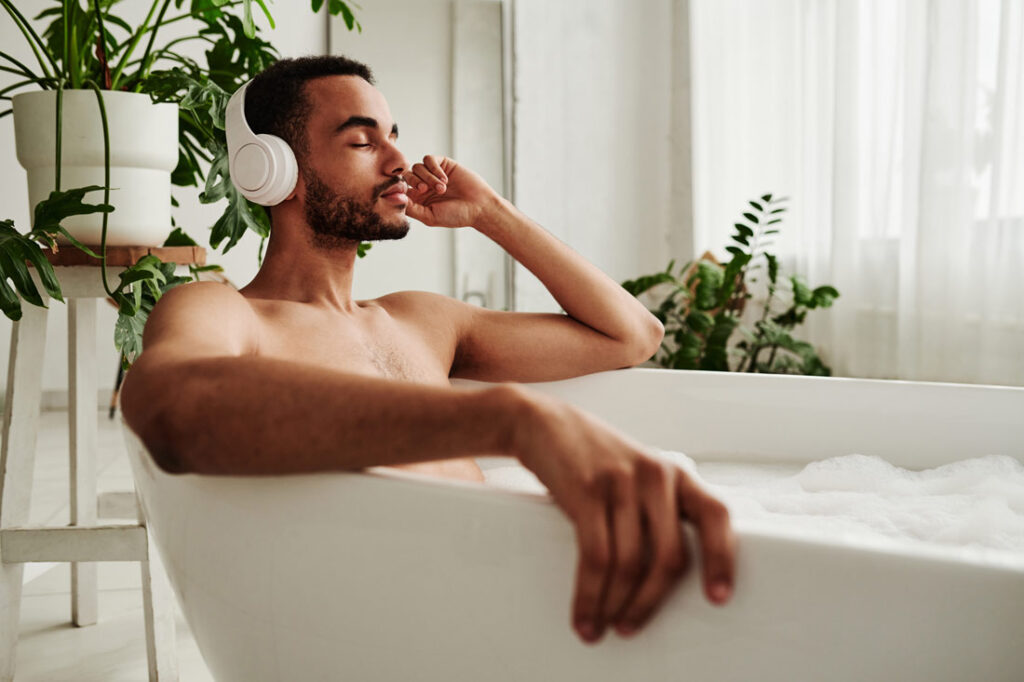 Man taking a bath with headphones on learning the importance of sustainable self care