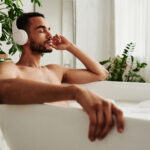 Man taking a bath with headphones on learning the importance of sustainable self care