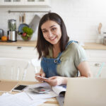 Woman sitting in her kitchen planning her short term financial goals and smiling