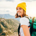 Female backpacker with mountains in the background smiling because she knows the best places to travel solo