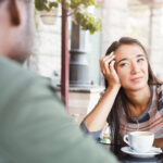 Woman with empathy fatigue trying to pay attention to a conversation over coffee but failing