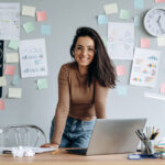 Woman at her work desk with sticky notes on the wall behind her because she's learning how to set goals at work