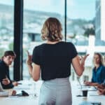 Rear view of a woman speaking to a group of employees at a conference table