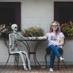 Amy Pickard, who throws death parties, holding hands with a faux skeleton at a bistro table