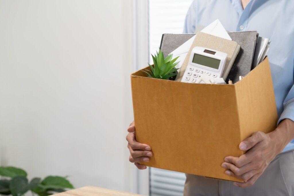 An employee carries a cardboard box full of office supplies.