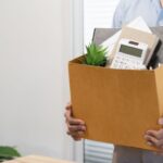 An employee carries a cardboard box full of office supplies.