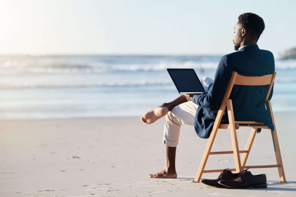 On the beach, a young man in a suit working on his laptop looks out over the ocean