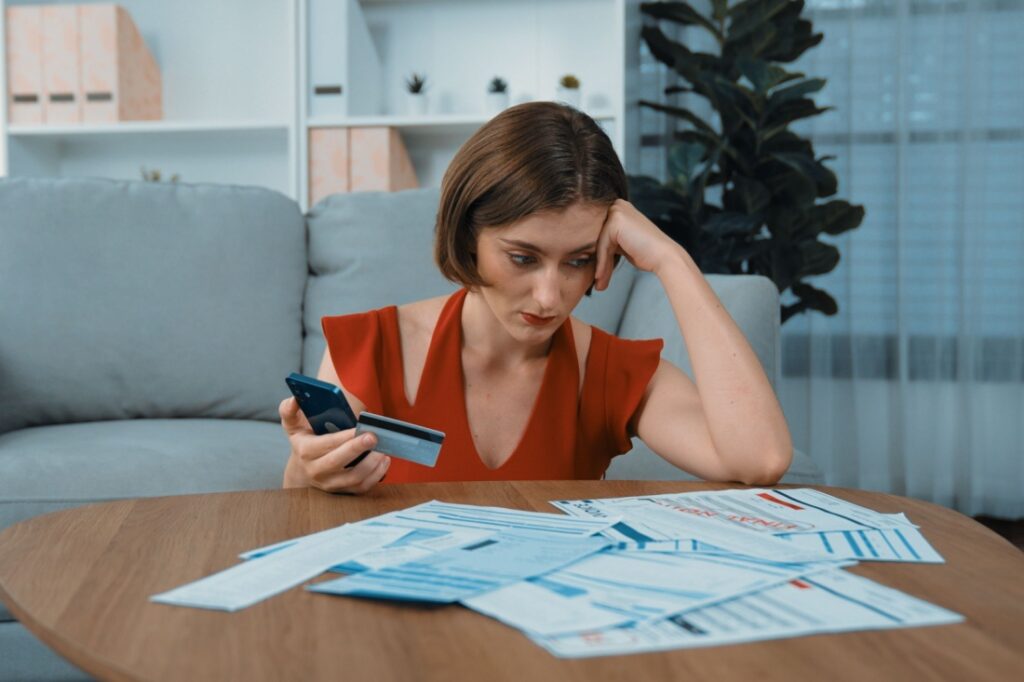 A woman looks down at a pile of bills on her coffee table.