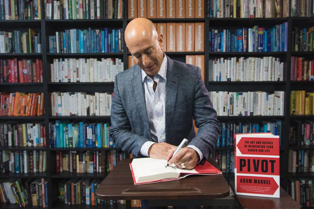 Author Adam Markel in signing a copy of his book, Pivot, in front of a bookcase.