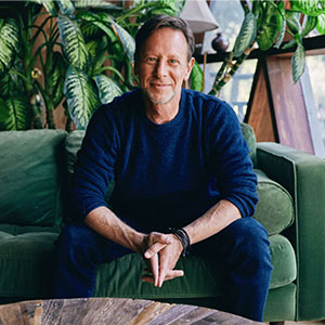 man with sitting on green couch with blue sweater and plant in backdrop