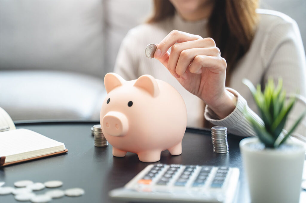 Young woman saving money monthly expenses putting coin in to piggy bank on the table.