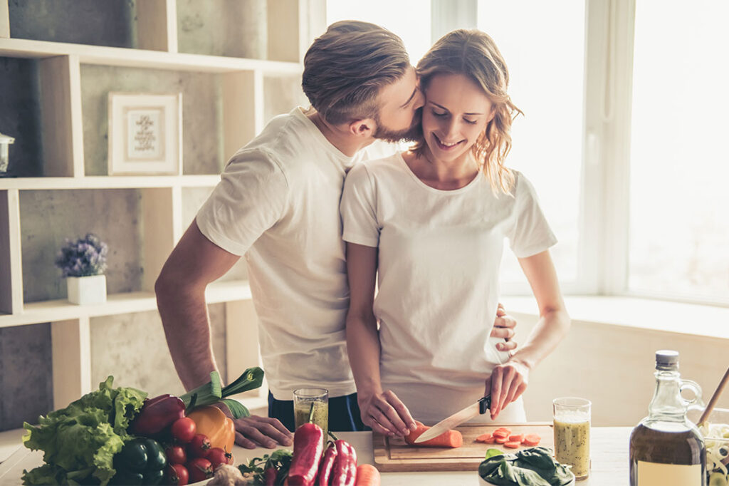 young couple is talking and smiling while cooking healthy food in kitchen at home.