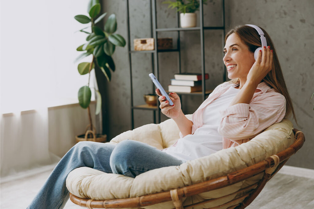 Young woman wears casual clothes sits in armchair with headphones