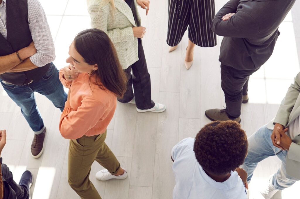 A woman in an orange shirt talks to a group of people.