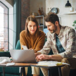 Couple using laptop computer, sitting on sofa in apartment