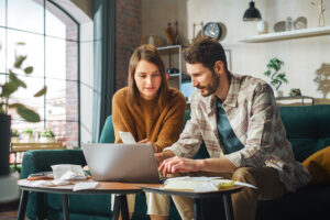 Couple using laptop computer, sitting on sofa in apartment