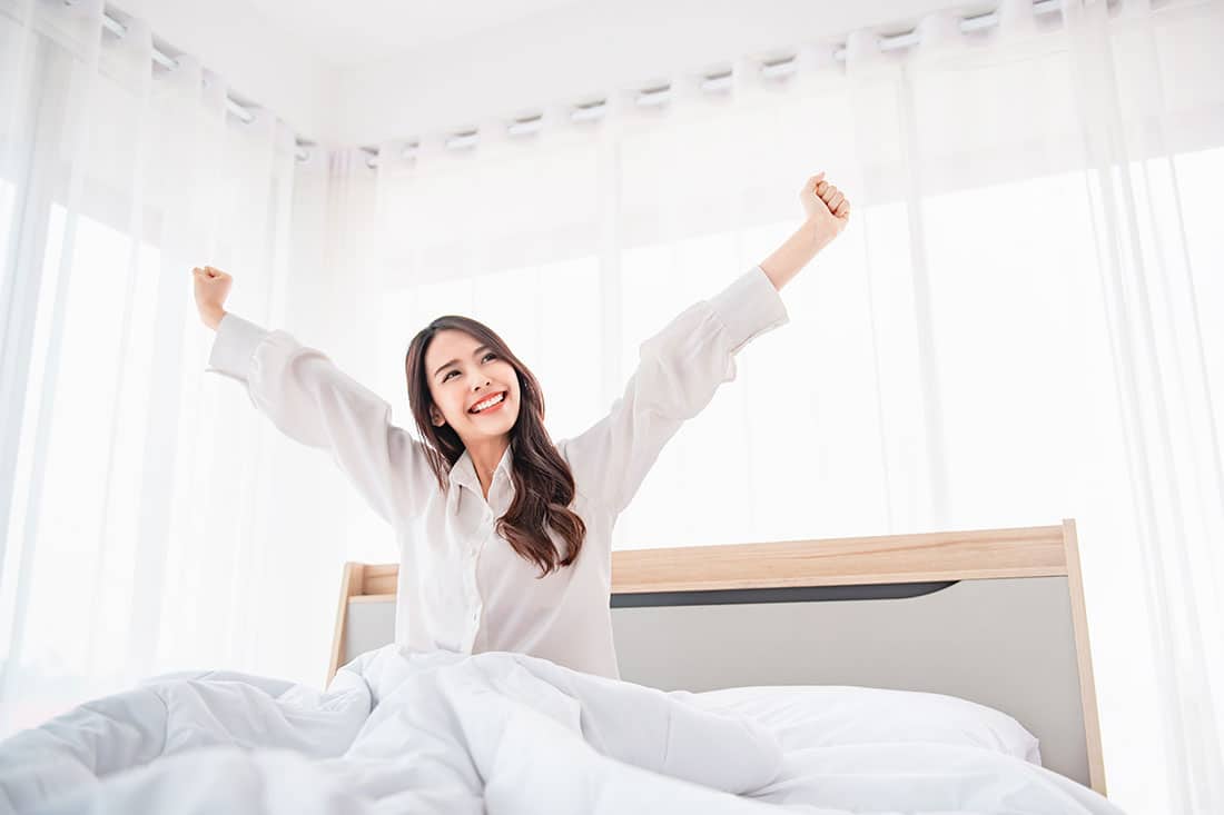 Happy asian woman stretching hands in bed after wake up in the morning