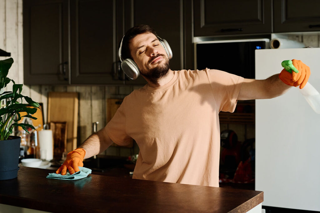 Young man in headphones enjoying music with headphones while standing by kitchen counter and cleaning